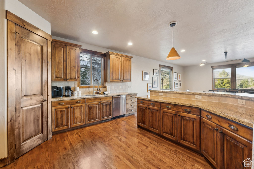 Kitchen with light stone counters, a sink, recessed lighting, wood finished floors, and stainless steel dishwasher