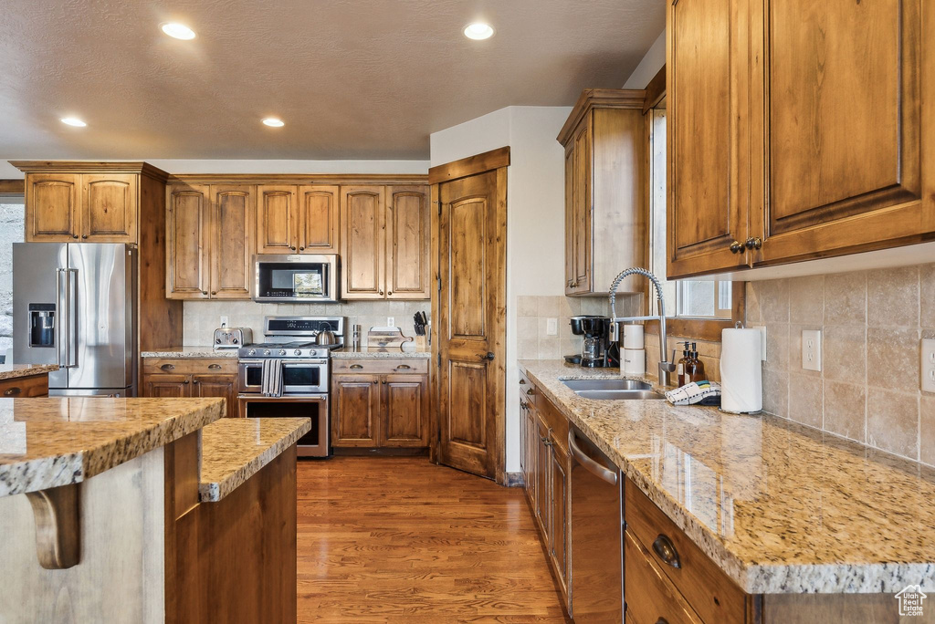 Kitchen featuring appliances with stainless steel finishes, a sink, brown cabinetry, decorative backsplash, and dark wood-style floors