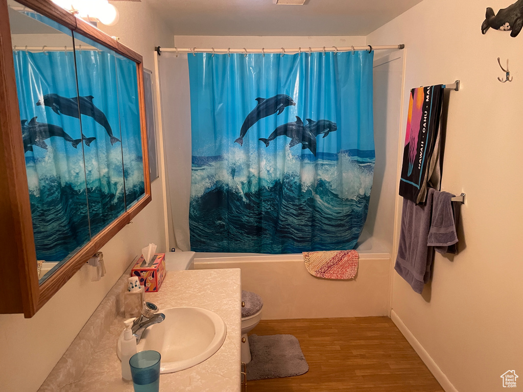 Full bath featuring vanity, shower / tub combo with curtain, wood finished floors, and toilet