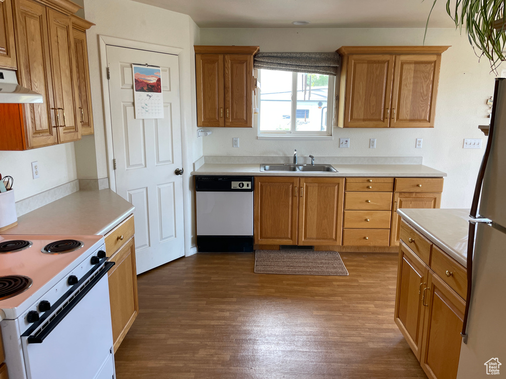Kitchen with dark wood-style flooring, white appliances, light countertops, under cabinet range hood, and a sink