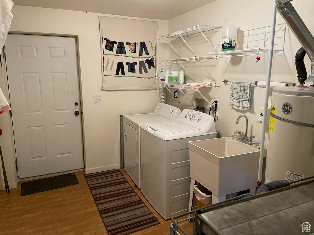 Clothes washing area with strapped water heater, laundry area, wood finished floors, and washing machine and clothes dryer