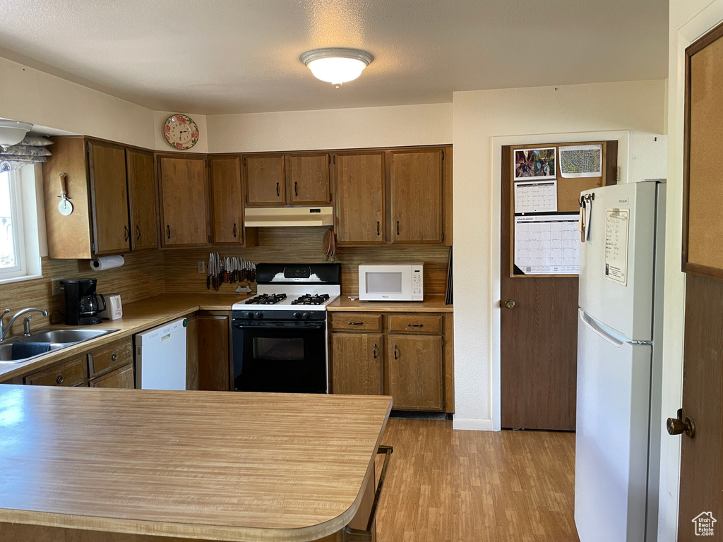 Kitchen featuring decorative backsplash, white appliances, light wood-style floors, under cabinet range hood, and a sink