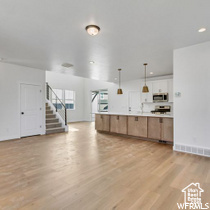 Kitchen featuring stainless steel microwave, open floor plan, hanging light fixtures, and light wood finished floors