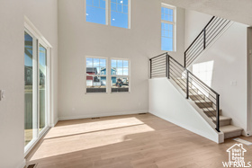 Unfurnished living room with baseboards, stairs, a towering ceiling, and wood finished floors