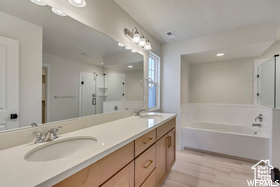 Bathroom featuring a sink, double vanity, wood finished floors, a garden tub, and a stall shower