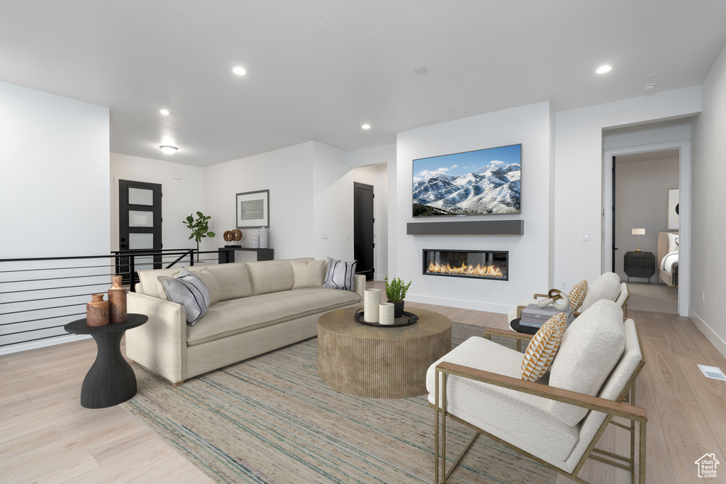 Living room with recessed lighting, light wood-style flooring, a glass covered fireplace, and baseboards