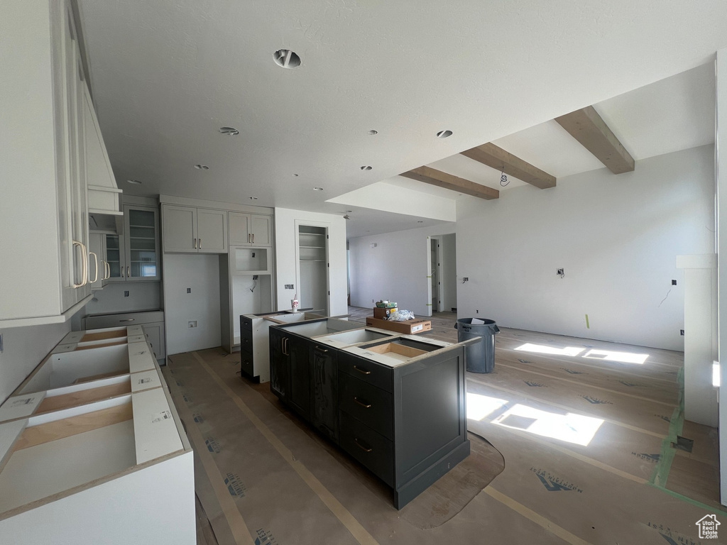 Kitchen with white cabinetry, dark cabinets, a center island, open floor plan, and beamed ceiling