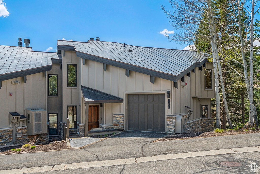 View of front of home featuring a garage, a standing seam roof, aphalt driveway, and stone siding