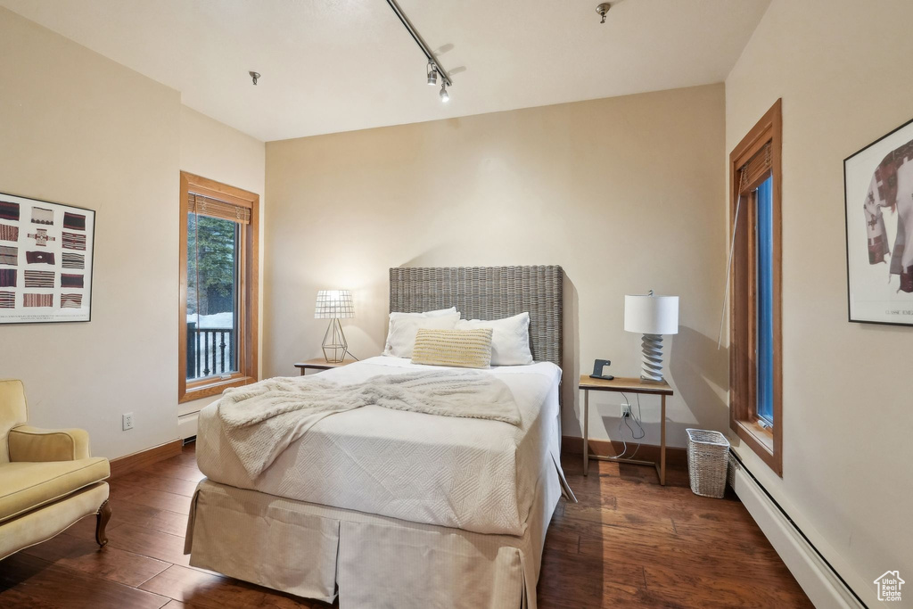 Bedroom with track lighting, baseboards, baseboard heating, dark wood finished floors, and a baseboard heating unit