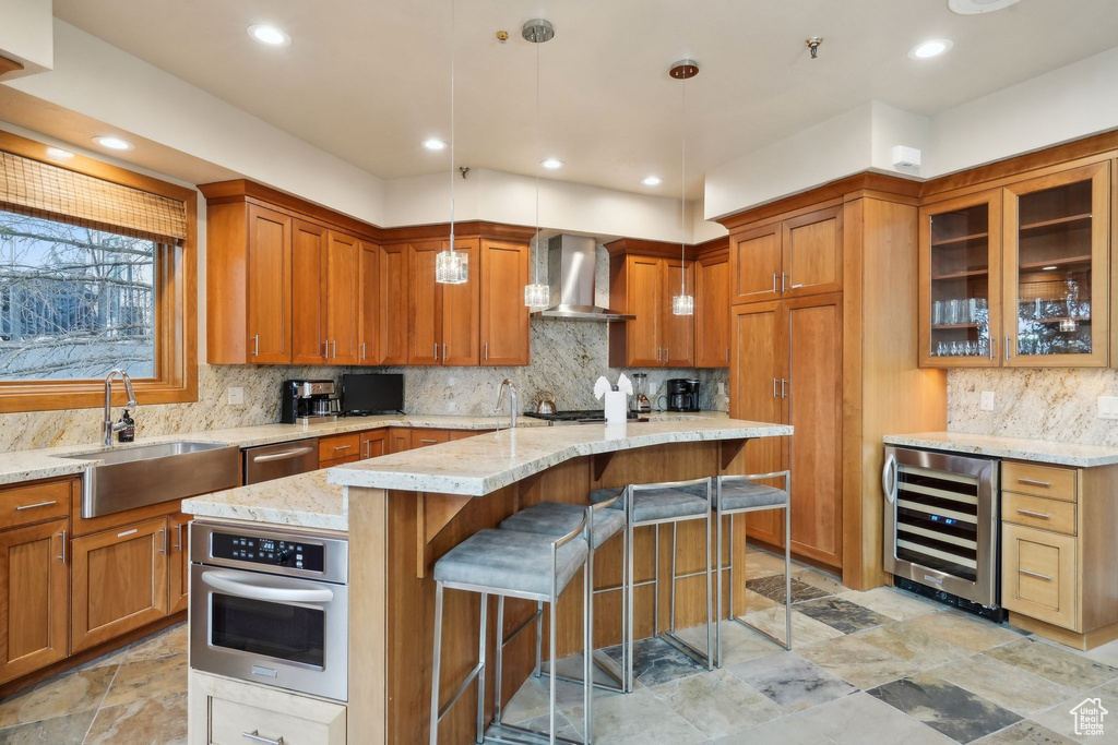 Kitchen featuring light stone countertops, stainless steel oven, wall chimney range hood, a sink, and wine cooler