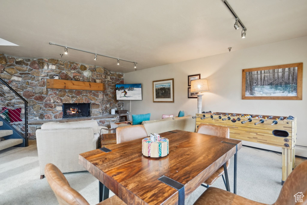 Dining area featuring rail lighting, stairs, a stone fireplace, and carpet floors