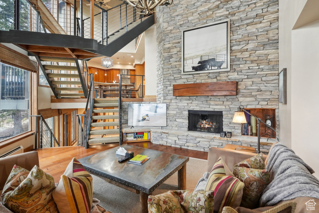 Living area with a fireplace, a high ceiling, stairs, a baseboard radiator, and wood finished floors
