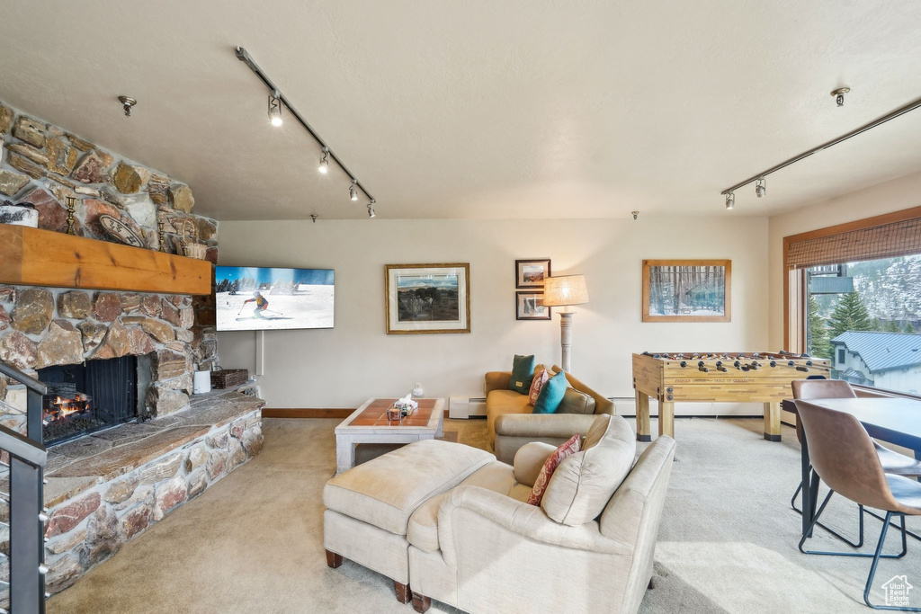 Carpeted living area with track lighting, a baseboard heating unit, baseboards, and a stone fireplace
