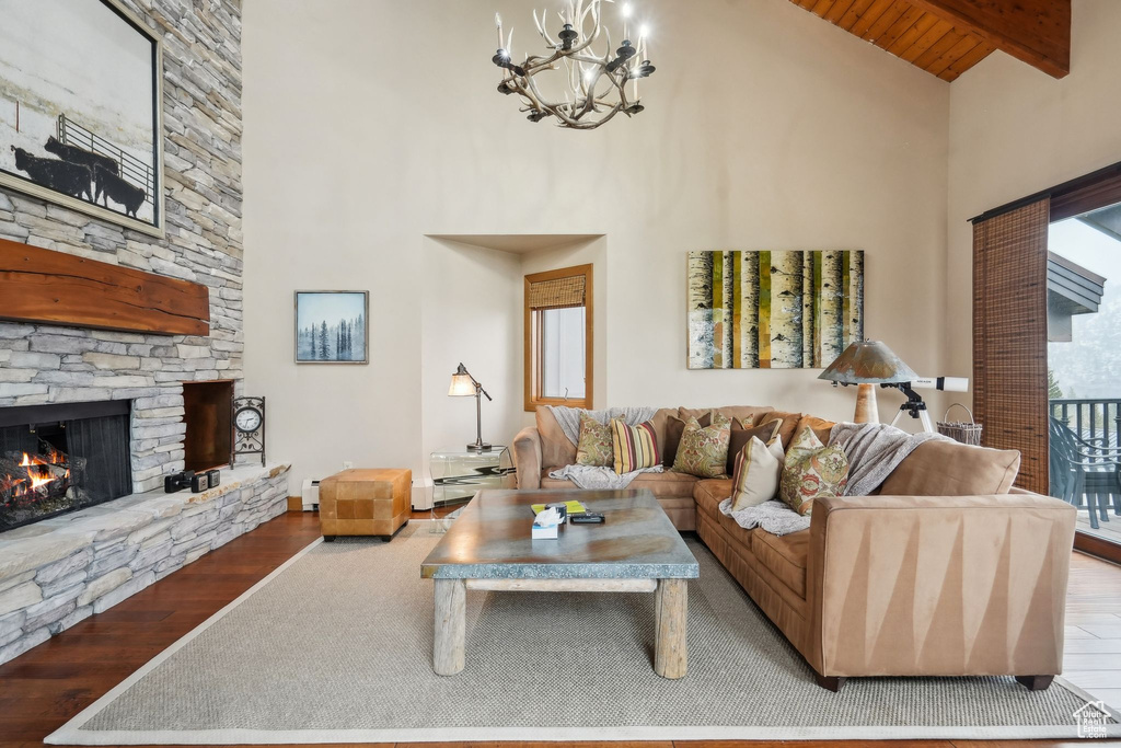 Living room featuring beam ceiling, a stone fireplace, high vaulted ceiling, and wood finished floors