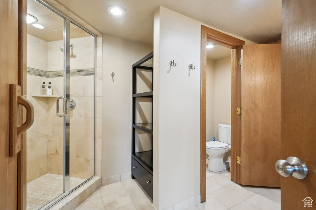 Full bath with tile patterned floors, toilet, a stall shower, and baseboards
