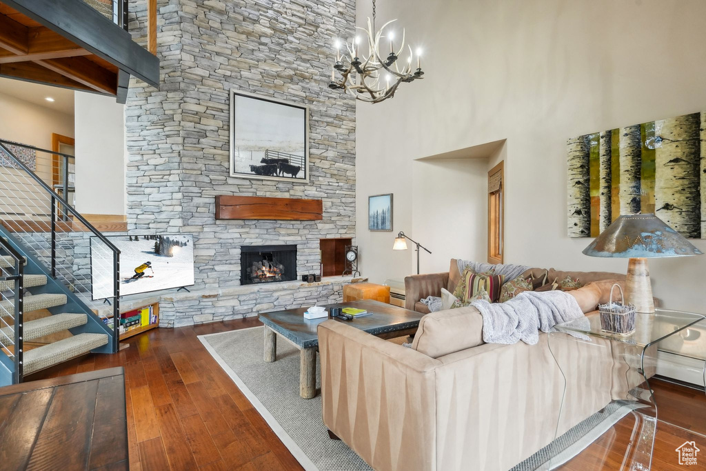 Living area featuring a towering ceiling, a stone fireplace, a chandelier, stairs, and wood-type flooring