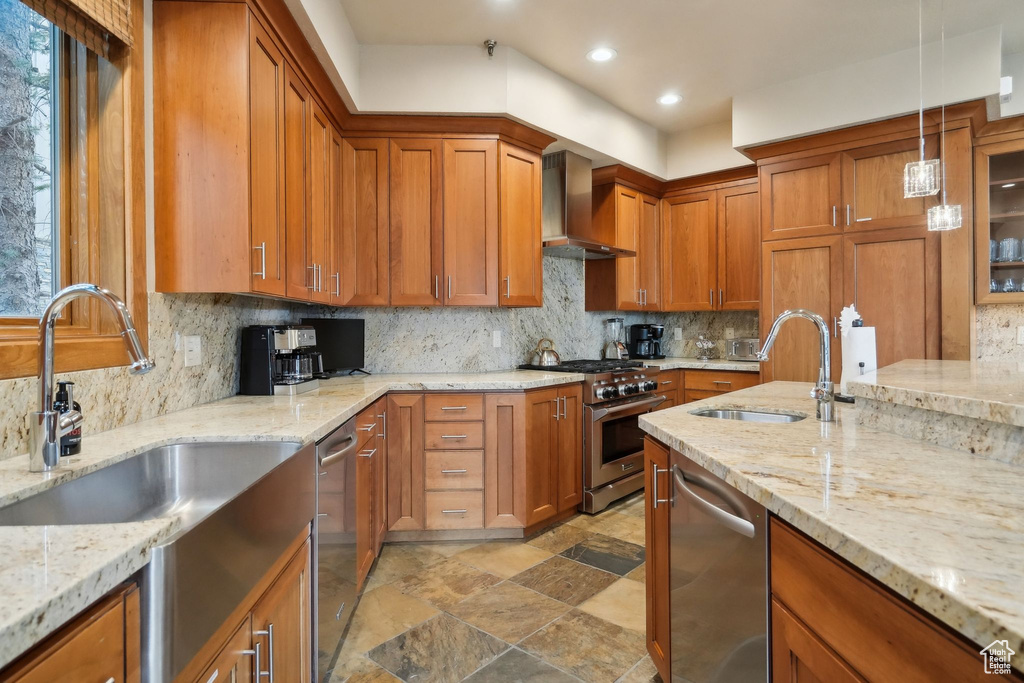 Kitchen with stainless steel appliances, brown cabinetry, wall chimney exhaust hood, and a sink
