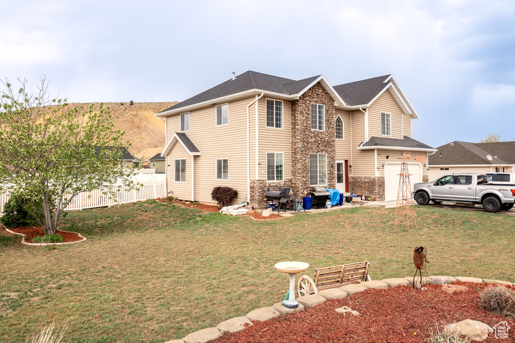 Exterior space with a lawn, an attached garage, fence, and stone siding