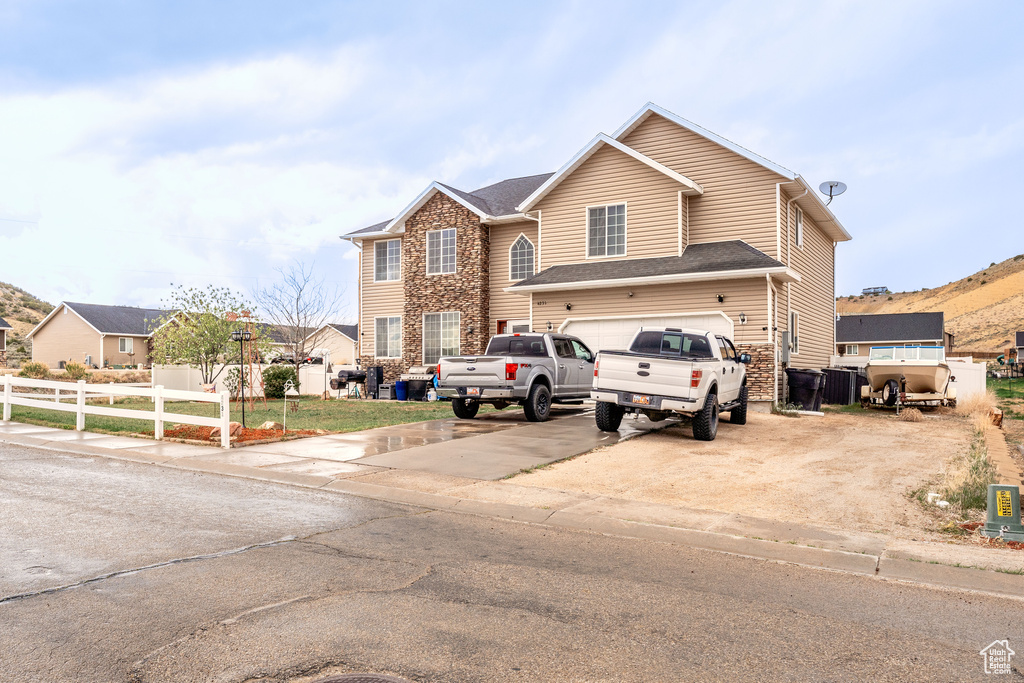 View of front of home featuring fence, driveway, stone siding, and a garage