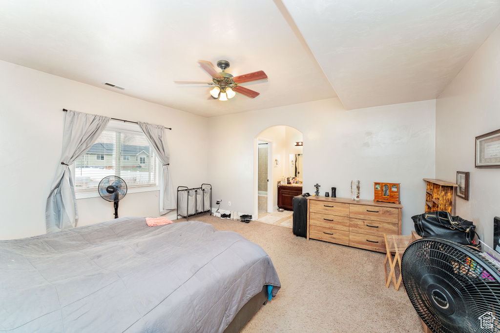Bedroom featuring a ceiling fan, visible vents, arched walkways, ensuite bathroom, and light carpet