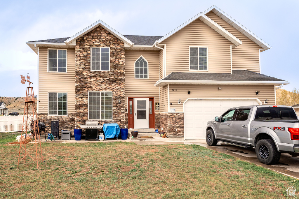 Rear view of property featuring an attached garage, stone siding, entry steps, a lawn, and driveway