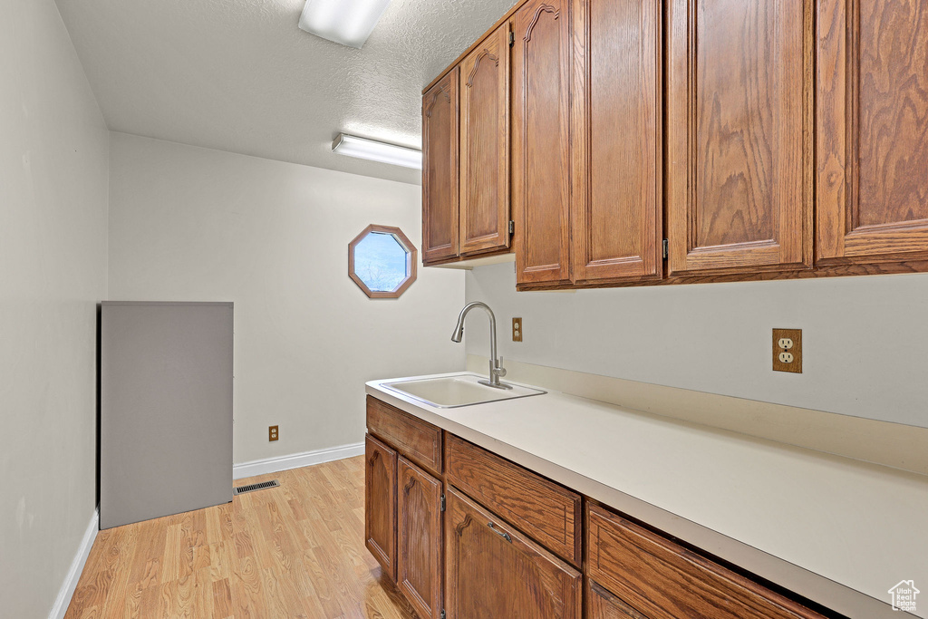 Kitchen featuring visible vents, baseboards, brown cabinets, a sink, and light wood finished floors