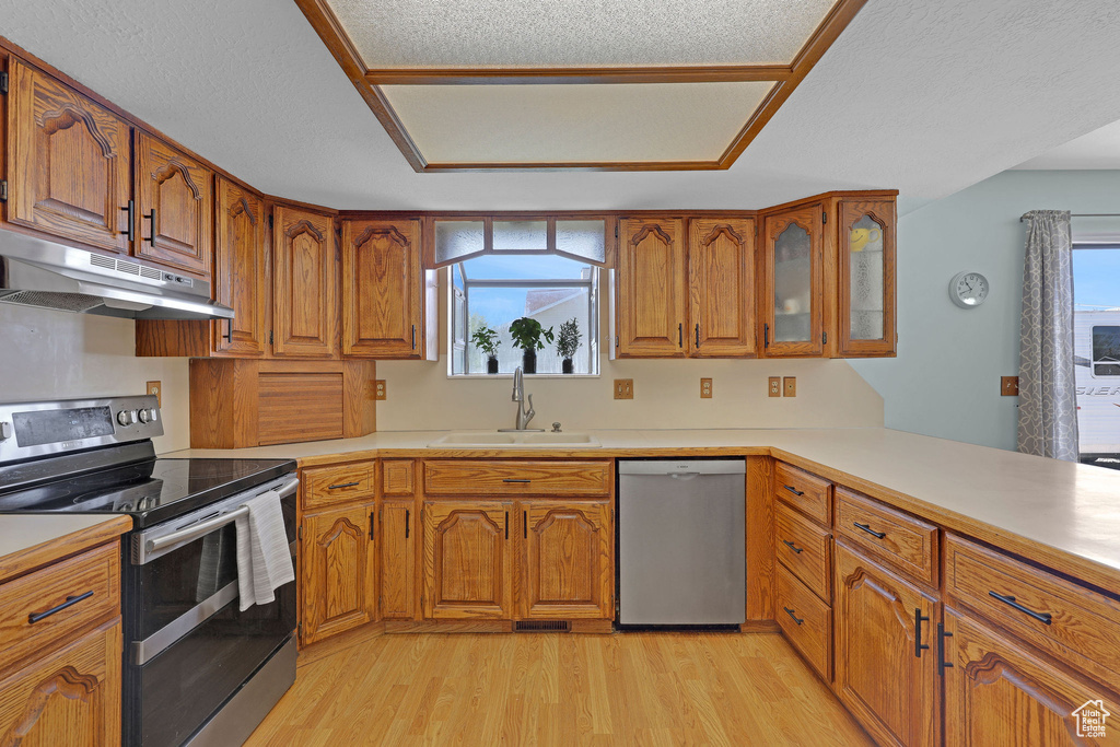 Kitchen with light wood-style floors, under cabinet range hood, brown cabinets, a sink, and appliances with stainless steel finishes