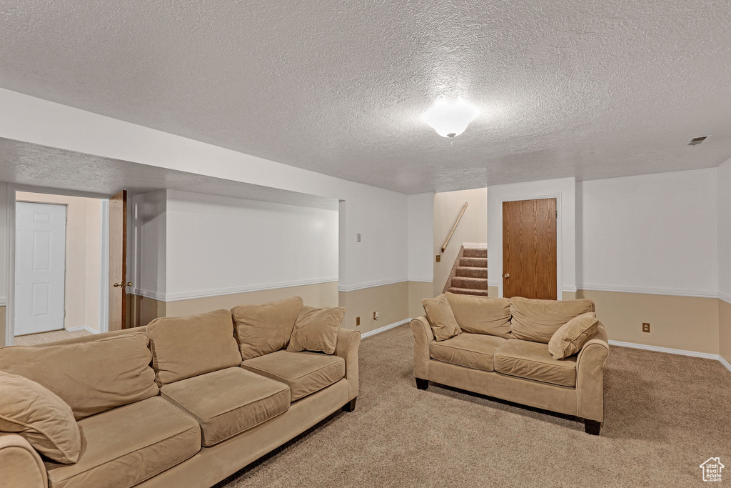 Living area featuring carpet floors, baseboards, stairs, and a textured ceiling