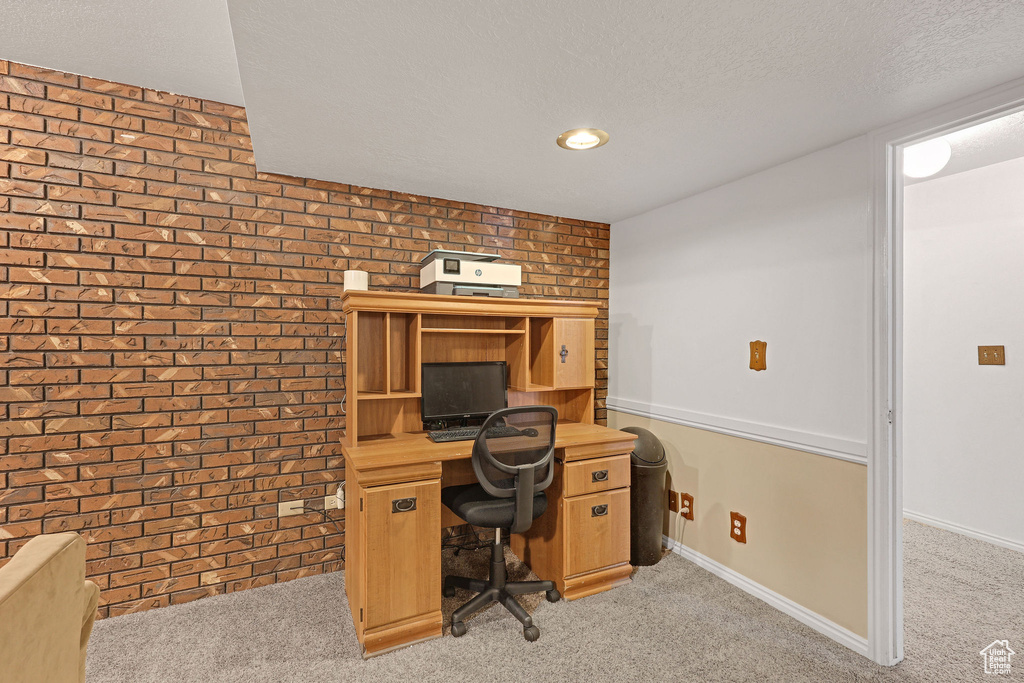 Office area featuring baseboards, light carpet, and brick wall