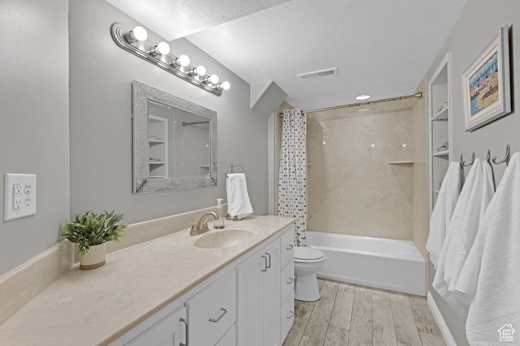 Bathroom with shower / bath combo, vanity, toilet, wood finished floors, and visible vents