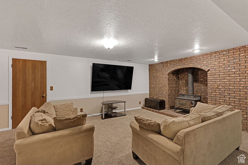 Carpeted living area featuring a textured ceiling, baseboards, a wood stove, and brick wall