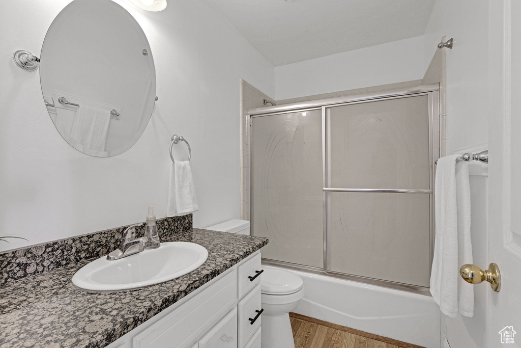 Full bathroom with toilet, enclosed tub / shower combo, wood finished floors, and vanity