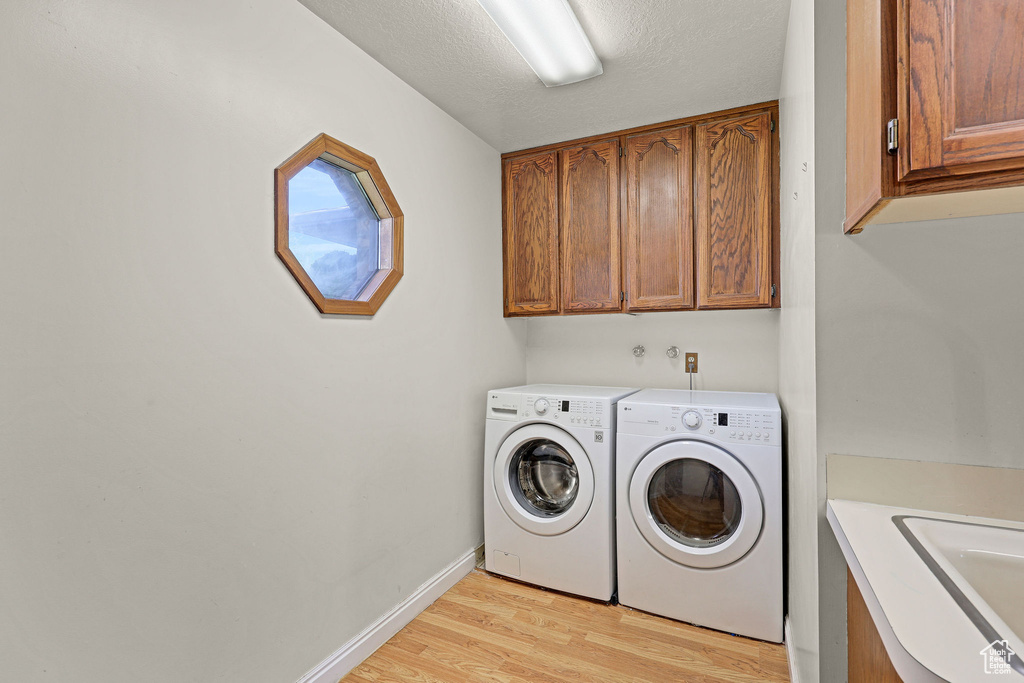 Laundry room featuring baseboards, washing machine and clothes dryer, a sink, cabinet space, and light wood finished floors
