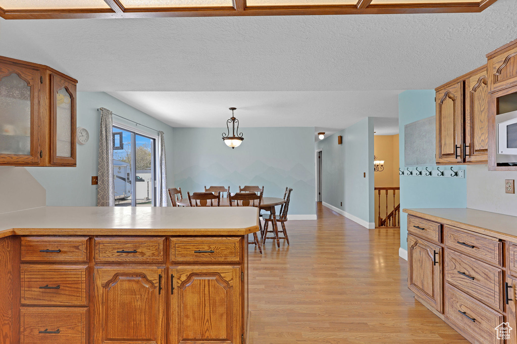 Kitchen featuring light wood-style floors, light countertops, brown cabinetry, and a peninsula