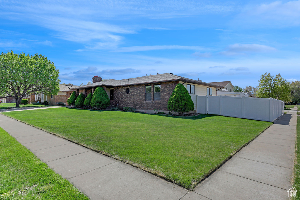 View of side of property with fence, a chimney, a lawn, and brick siding