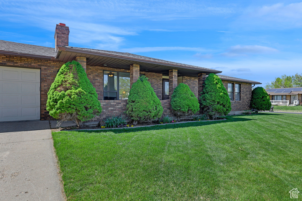 Ranch-style house with brick siding, an attached garage, a chimney, and a front yard