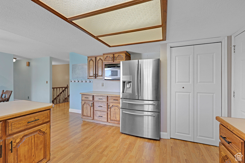 Kitchen with stainless steel refrigerator with ice dispenser, light countertops, light wood finished floors, and brown cabinetry