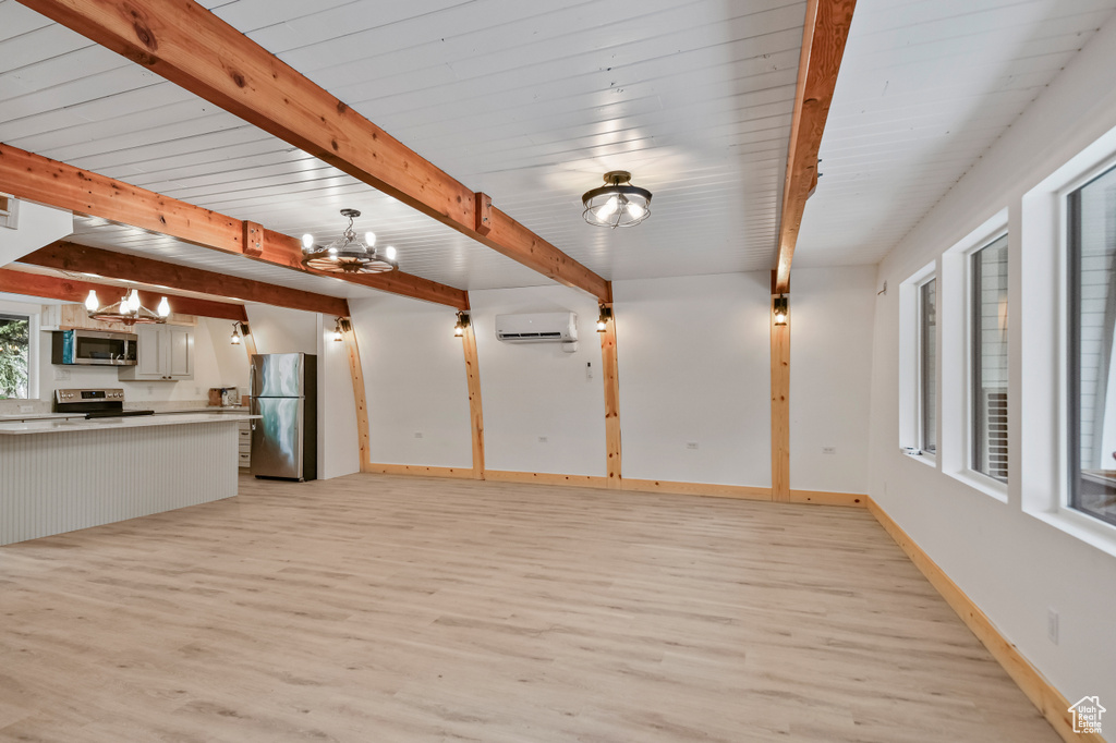 Unfurnished living room featuring beam ceiling, baseboards, an AC wall unit, a chandelier, and light wood-style floors