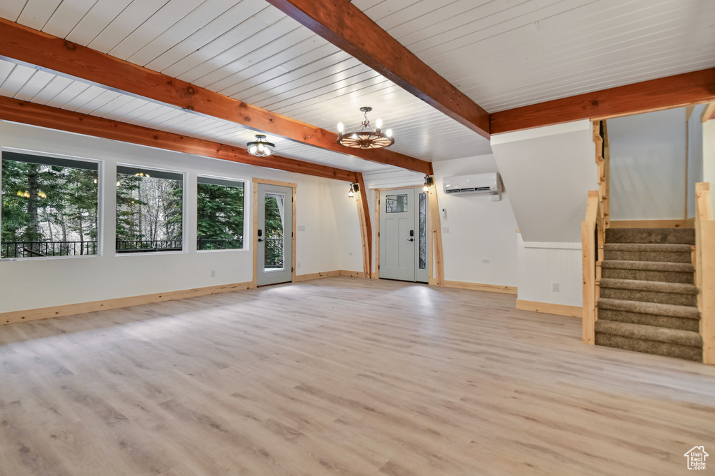 Unfurnished living room with a chandelier, a wall unit AC, a wealth of natural light, and light wood-style floors