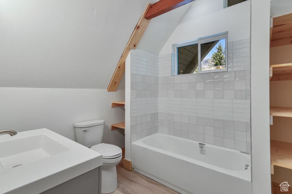 Bathroom featuring wood finished floors, lofted ceiling, toilet, a tub, and a sink