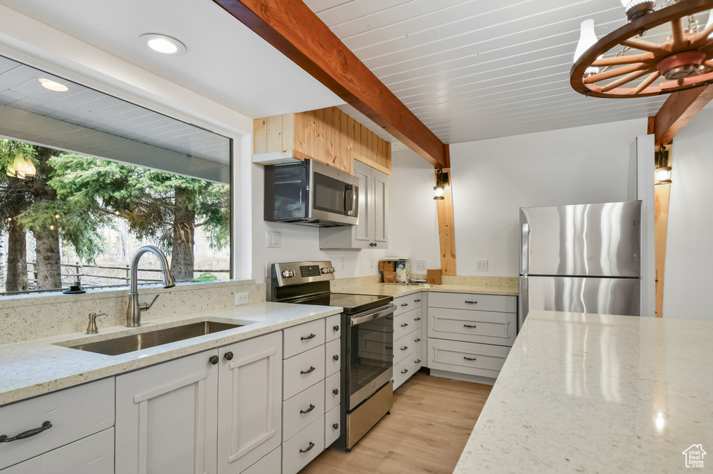 Kitchen with beam ceiling, light stone counters, a sink, light wood finished floors, and appliances with stainless steel finishes