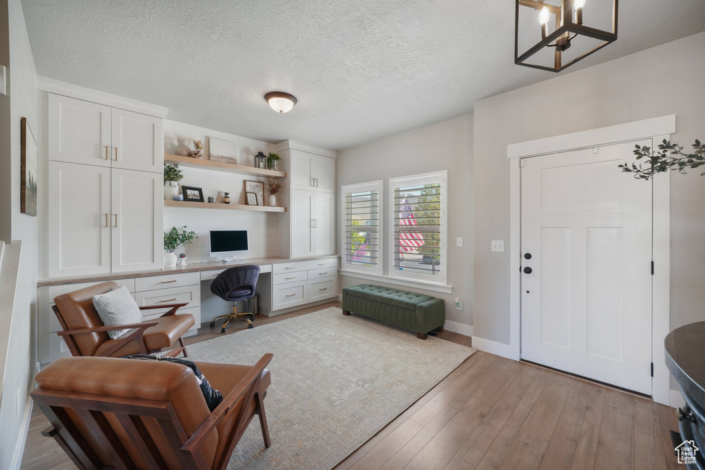 Office featuring a textured ceiling, built in study area, baseboards, a chandelier, and light wood-style flooring