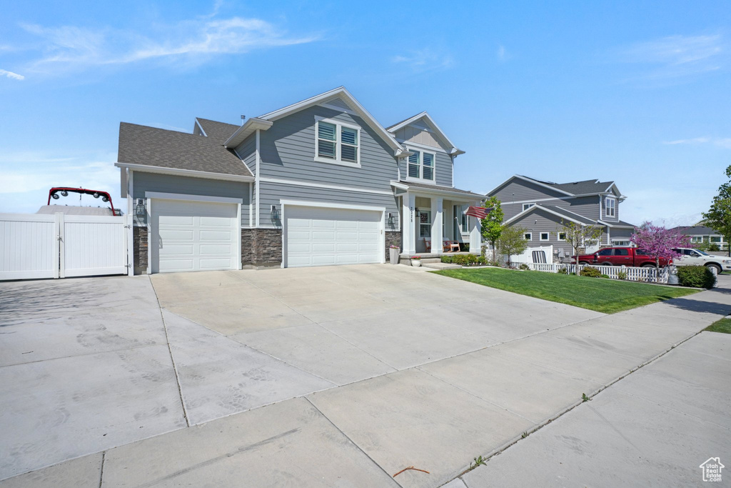 View of front of property featuring fence, a front lawn, stone siding, a gate, and concrete driveway