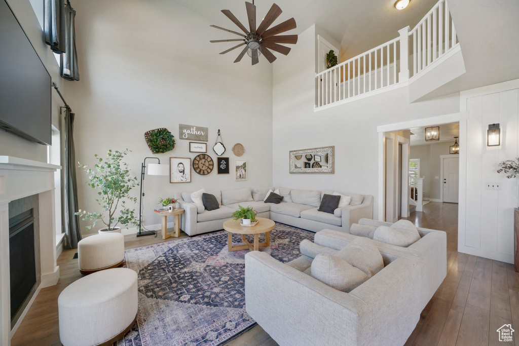 Living room featuring a high ceiling, ceiling fan, a fireplace, baseboards, and wood finished floors