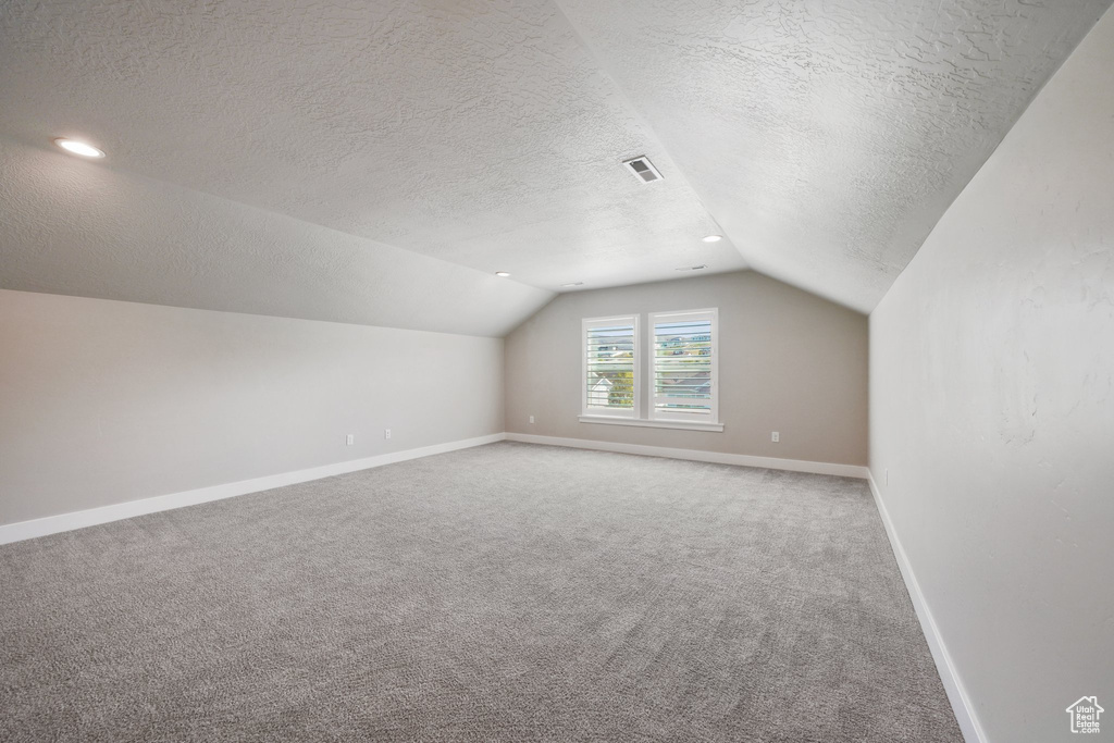 Bonus room with visible vents, carpet floors, a textured ceiling, baseboards, and vaulted ceiling