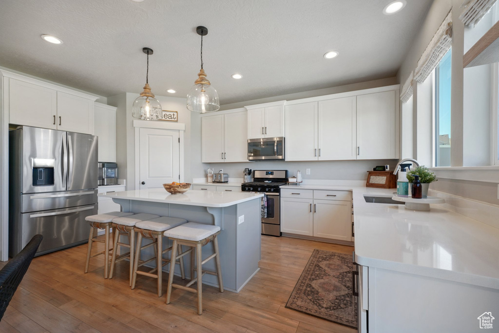 Kitchen with a kitchen island, a breakfast bar area, light countertops, white cabinetry, and appliances with stainless steel finishes