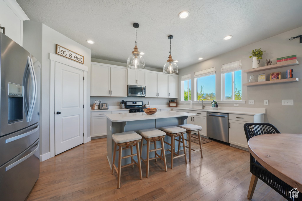 Kitchen with a sink, light countertops, a kitchen breakfast bar, stainless steel appliances, and white cabinetry