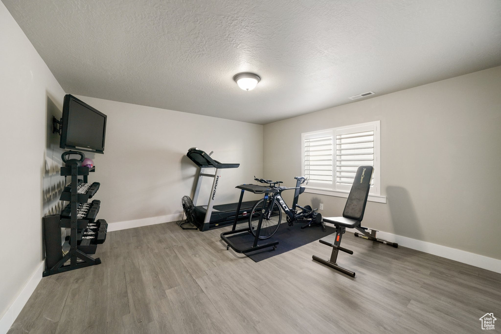 Workout area with visible vents, a textured ceiling, baseboards, and wood finished floors