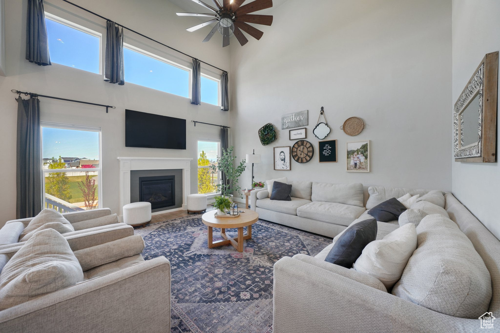 Living room featuring a ceiling fan, a high ceiling, and a glass covered fireplace