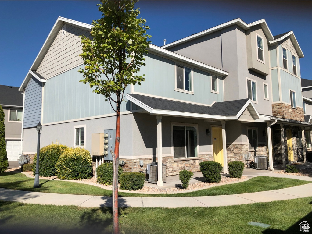 View of property with central AC unit, a front yard, and stone siding